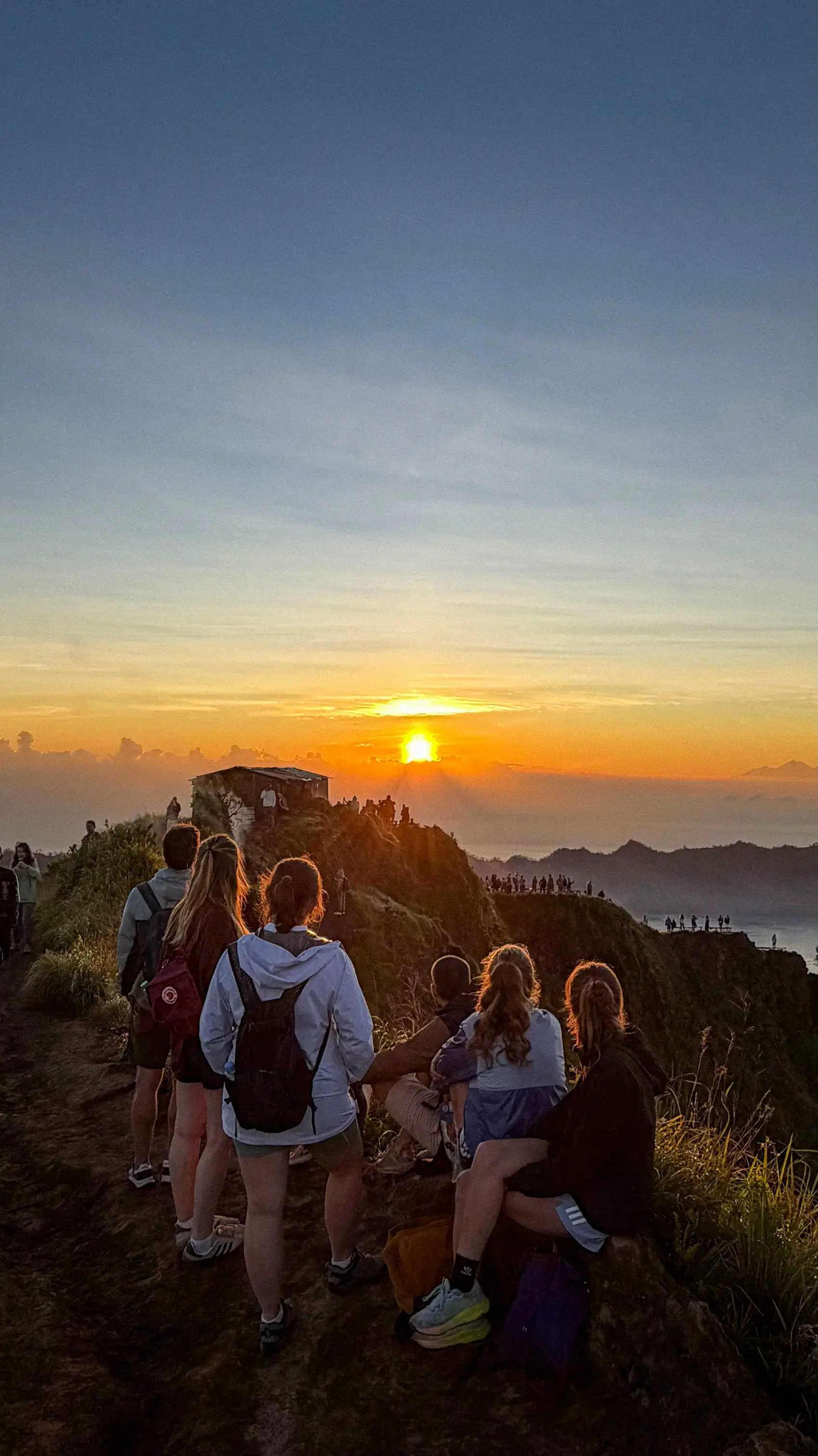 Un grupo sentado en una cima, mirando el amanecer sobre las montañas