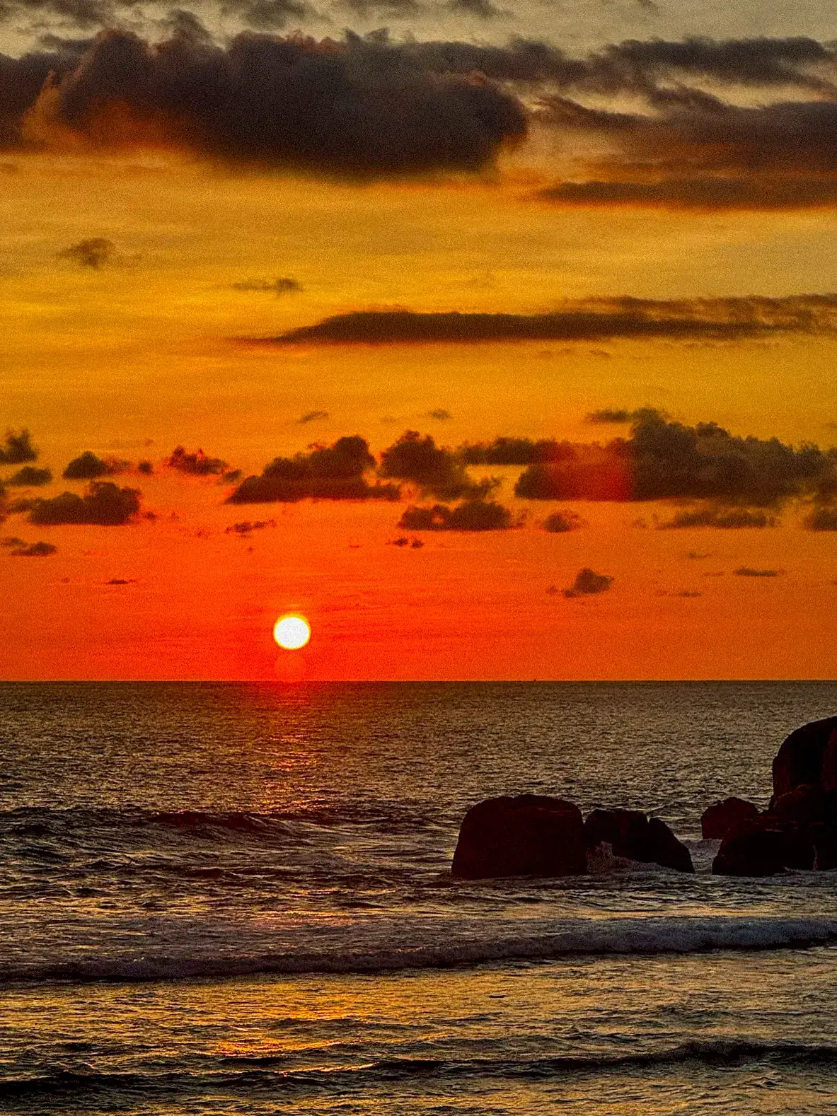 Atardecer naranja sobre el mar, con el sol cayendo entre las nubes