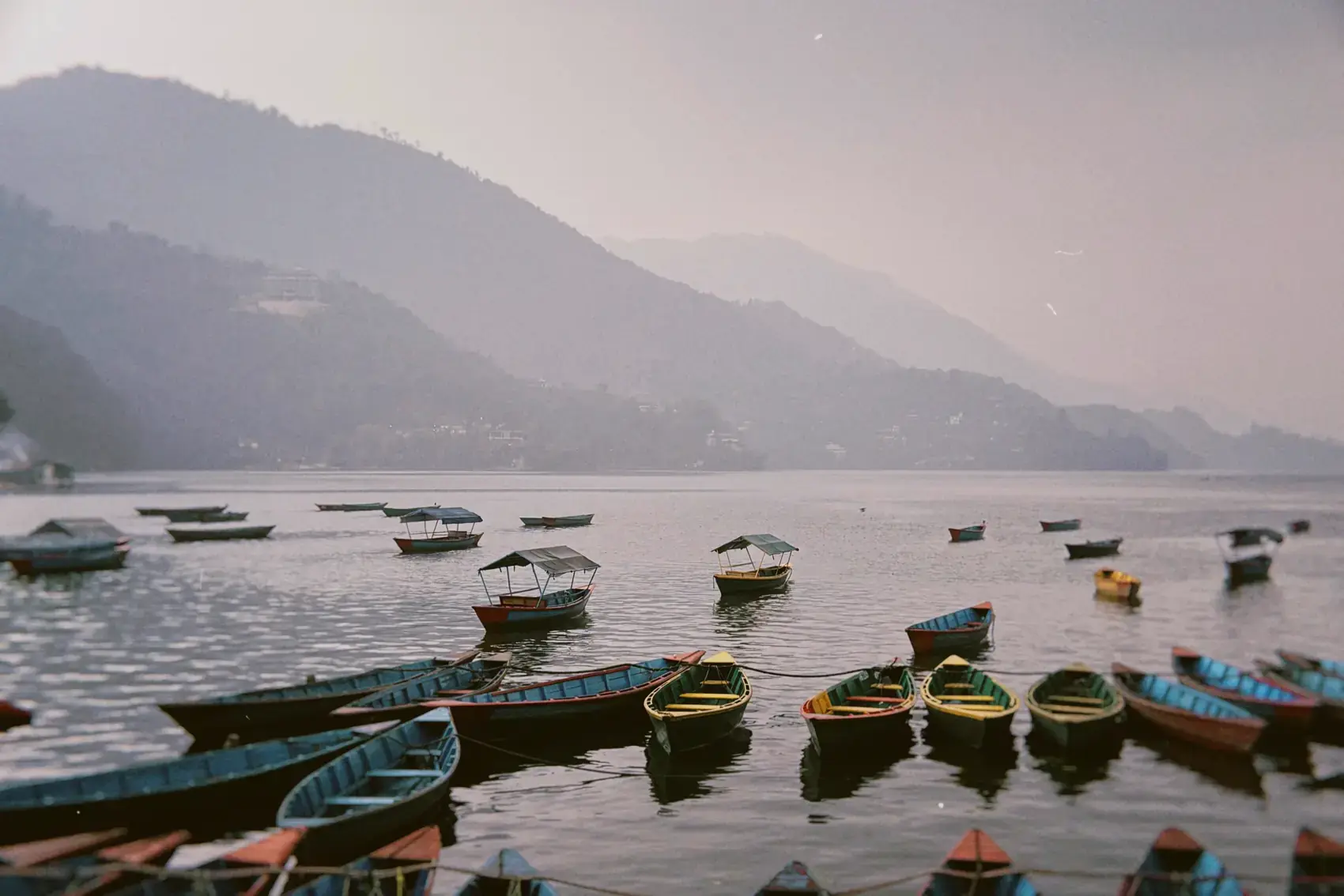 Botes de colores amarrados en el lago Phewa, con las montañas entre la bruma
