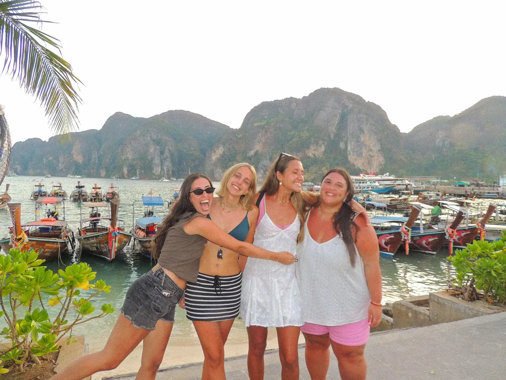 Cuatro viajeras abrazadas en el muelle de Phi Phi, con la fila de longtails atrás